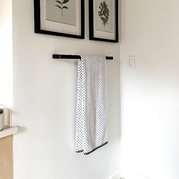 black towel bar in white bathroom with towel hanging and artwork above
