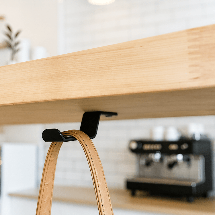 wood coffee bar with black purse hook under table holding brown bag