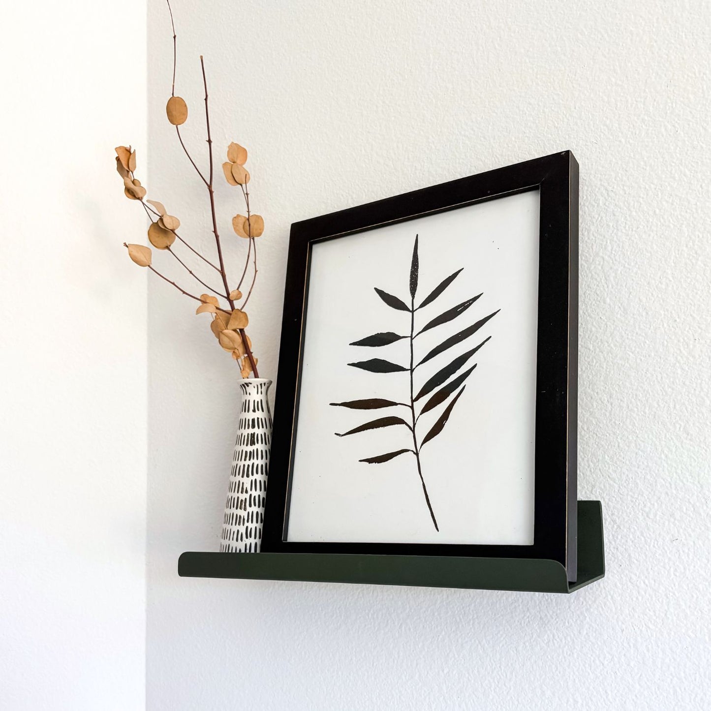wall mounted olive green ledge shelf with black and white print and vase with branch