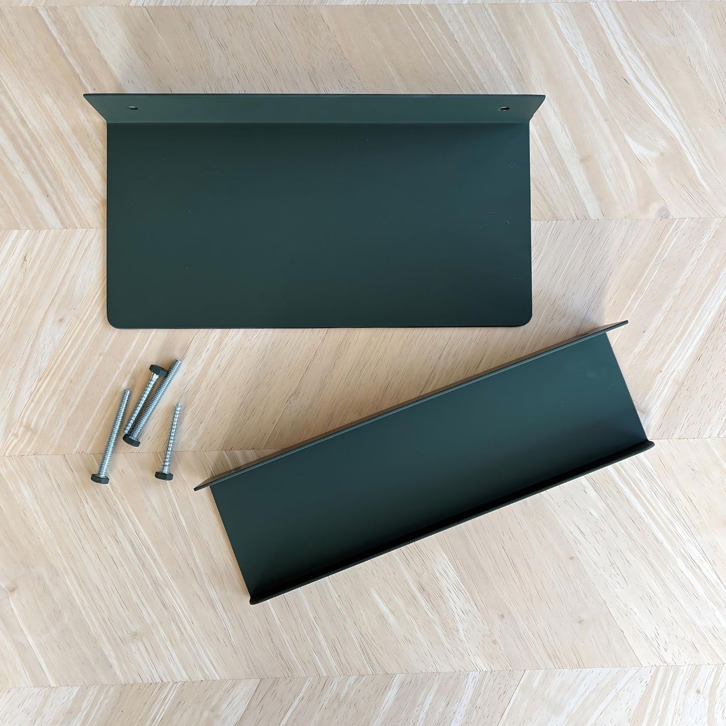 Two olive green shelves one a flat shelf and one a display ledge laying on a wood background. There are matching green bolts.
