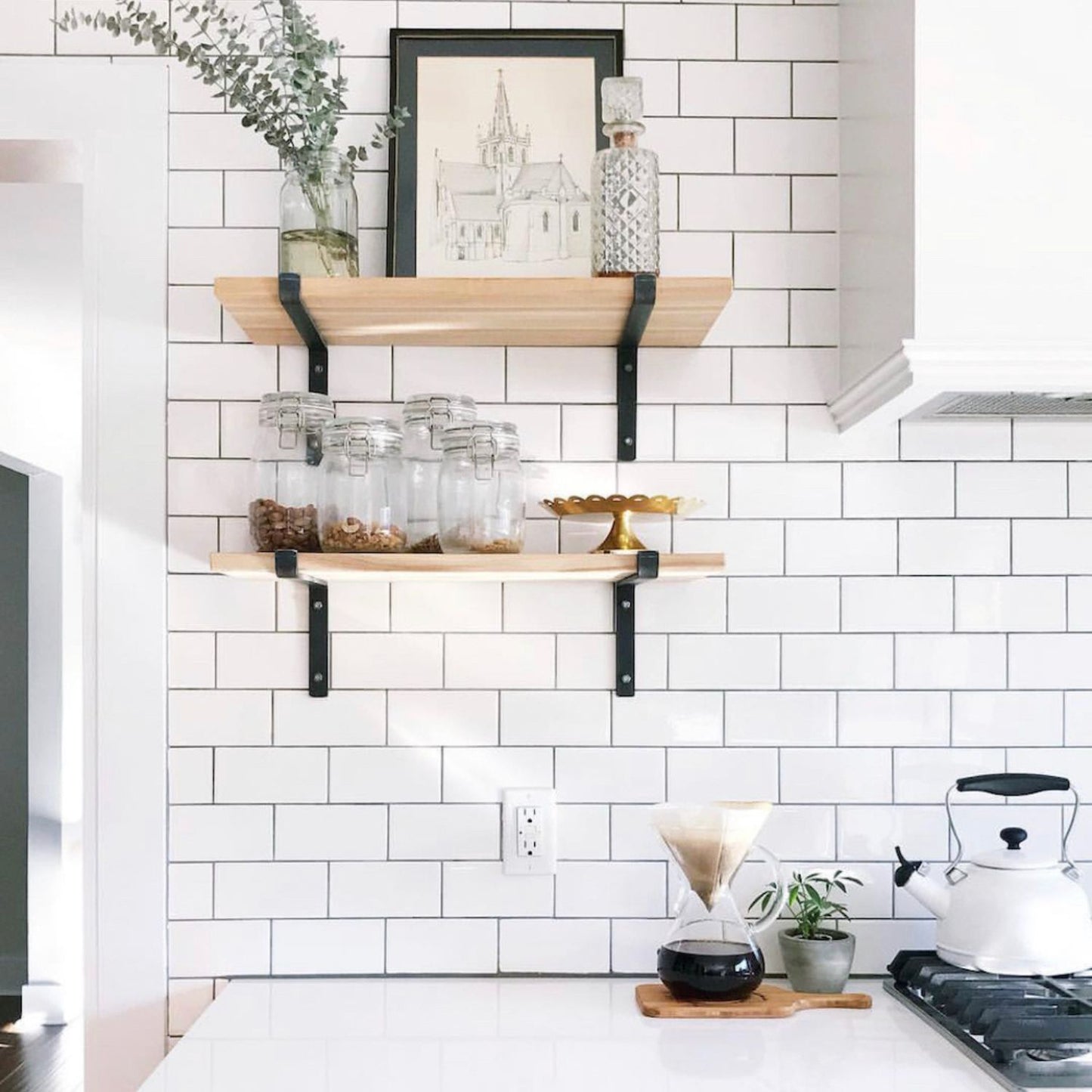 two wood shelves on white kitchen back splash tile support by black metal shelf brackets with decor