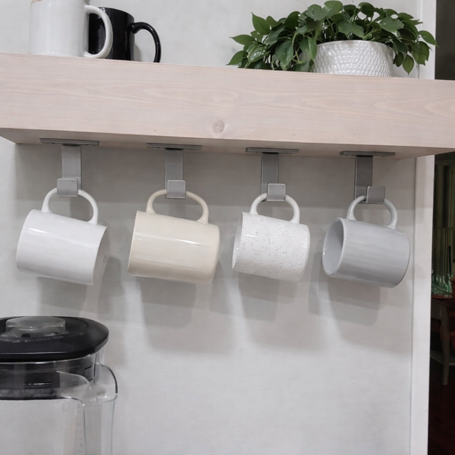 Kitchen with a wood shelf with four silver J hooks mounted underneath with four coffee mugs hanging.