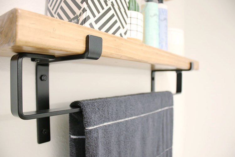 Bathroom with black metal towel bar mounted under a wood shelf hanging a hand towel. The shelf is supported by metal brackets