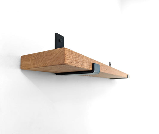 Wall shelf with oak shelf board installed with a metal J bracket onto a white wall. The shelf is empty