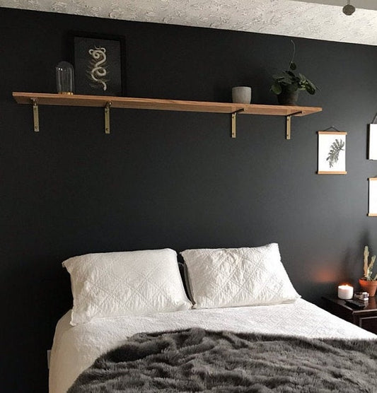 Bedroom with black wall and wood shelf above bed with metal brackets