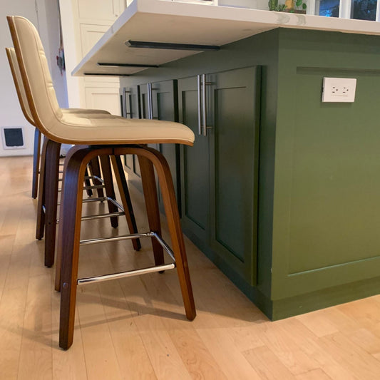 green kitchen cabinet island with white quartz countertop supported by minimal, hidden black brackets. There is a barstool.