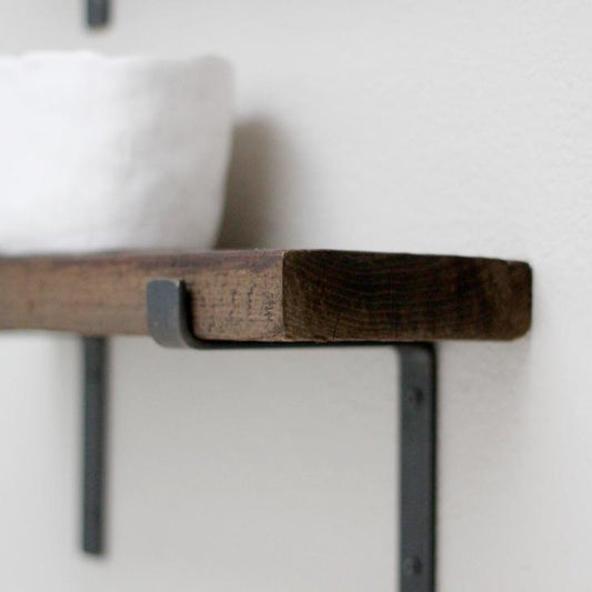 small wood shelf mounted on gray wall with raw steel z style shelf brackets. There is a white bowl on top