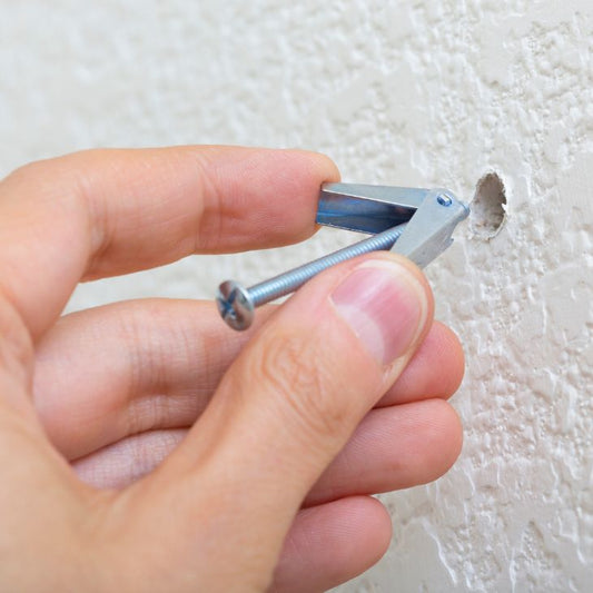 hand holding silver toggle bolt anchor and putting into drywall