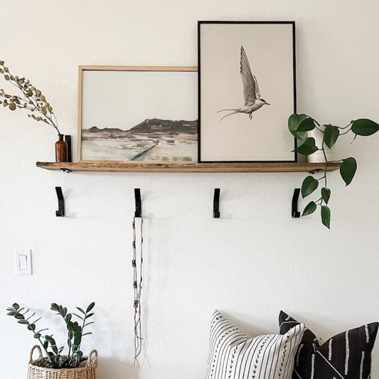 Entryway with wood shelf and four black wall hooks below. There is artwork and pillows on bench.
