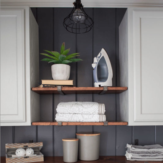 laundry room with two wood shelves and metal raw steel shelf brackets next to white cabinets with black wall
