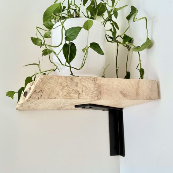 Square wood shelf with black corner shelf bracket installed onto white wall. There is a potted plant on top.