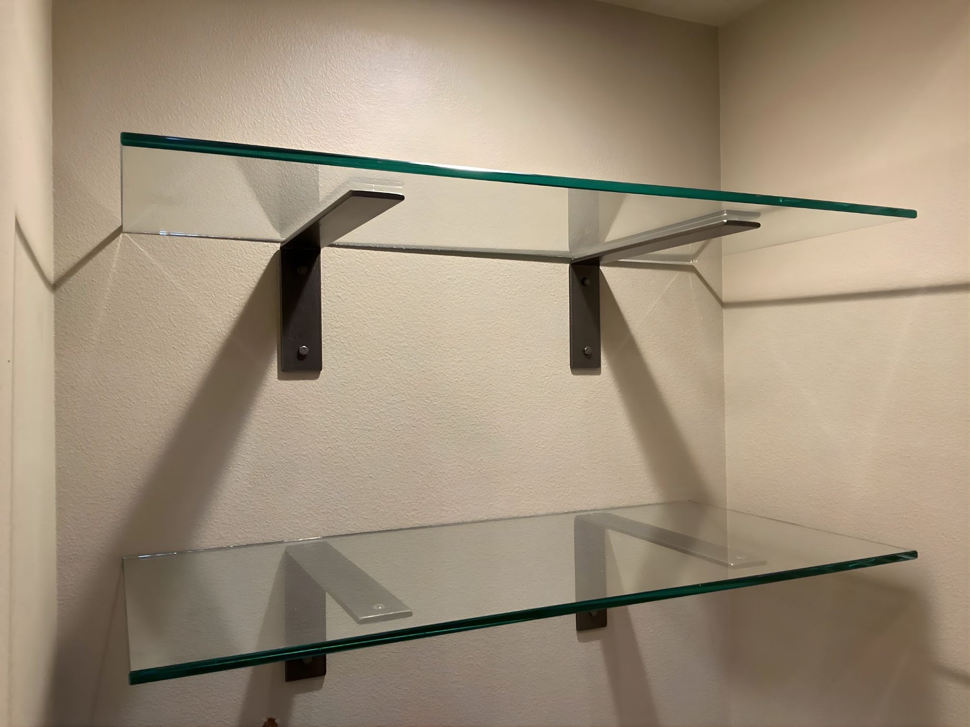 Glass shelves with metal brackets on a beige wall.