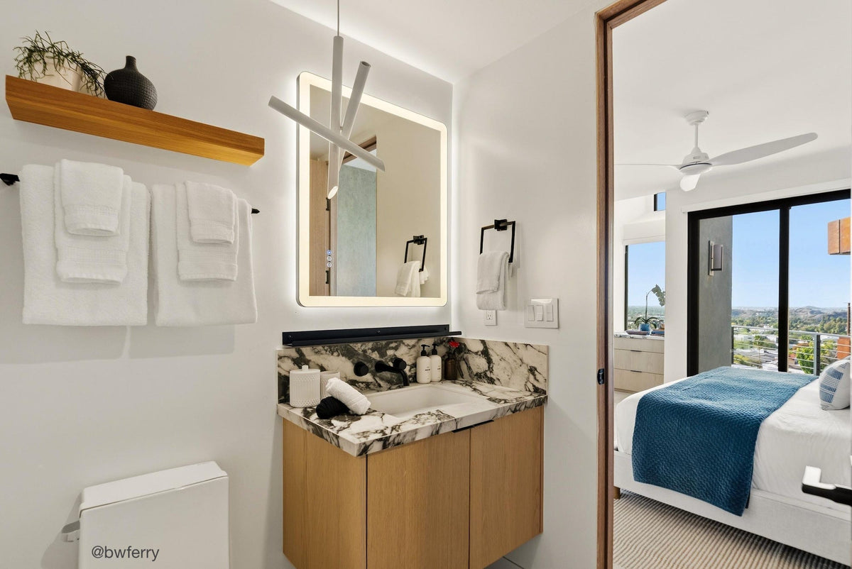 Bathroom with vanity and mirror and black shelf ledge for storage  leading to a bedroom with a bed and window.