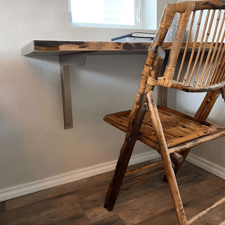 Home office with wood slab desk supported by angled heavy duty brass wall supports and woven chair