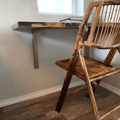 Home office with wood slab desk supported by angled heavy duty brass wall supports and woven chair