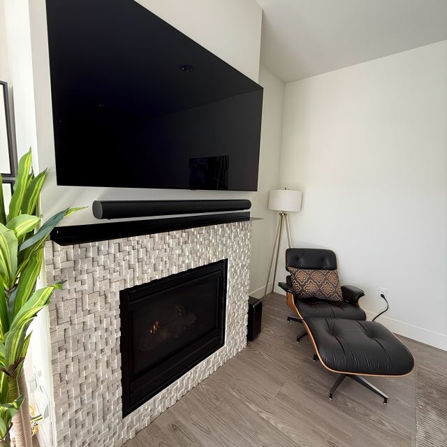 Modern living room with a fireplace with a floating metal mantel shelf, TV, and armchair.