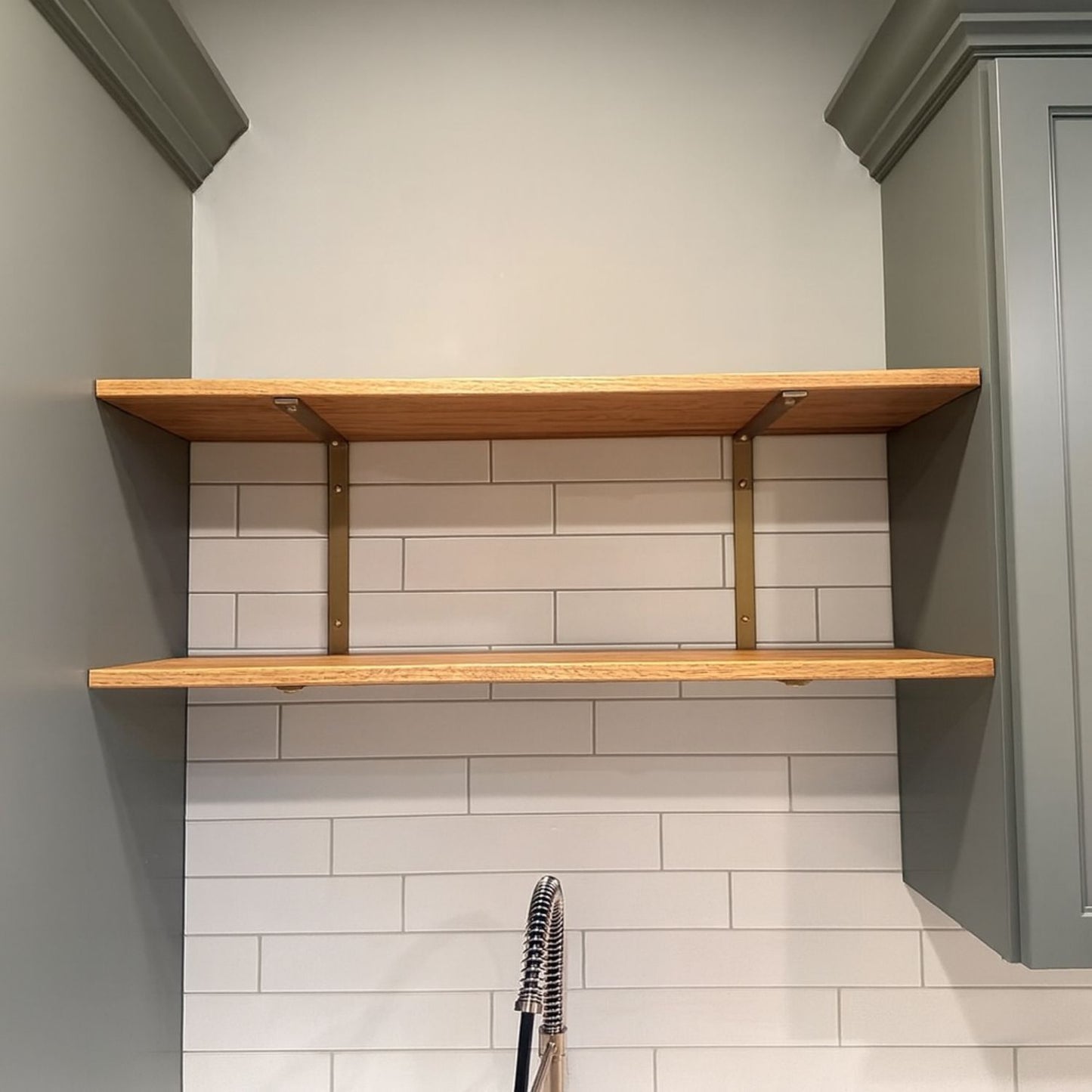 wood shelves with gold double brackets between green sage kitchen cabinets