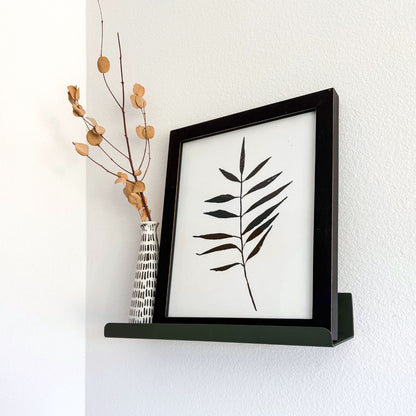 wall mounted olive green ledge shelf with black and white print and vase with branch