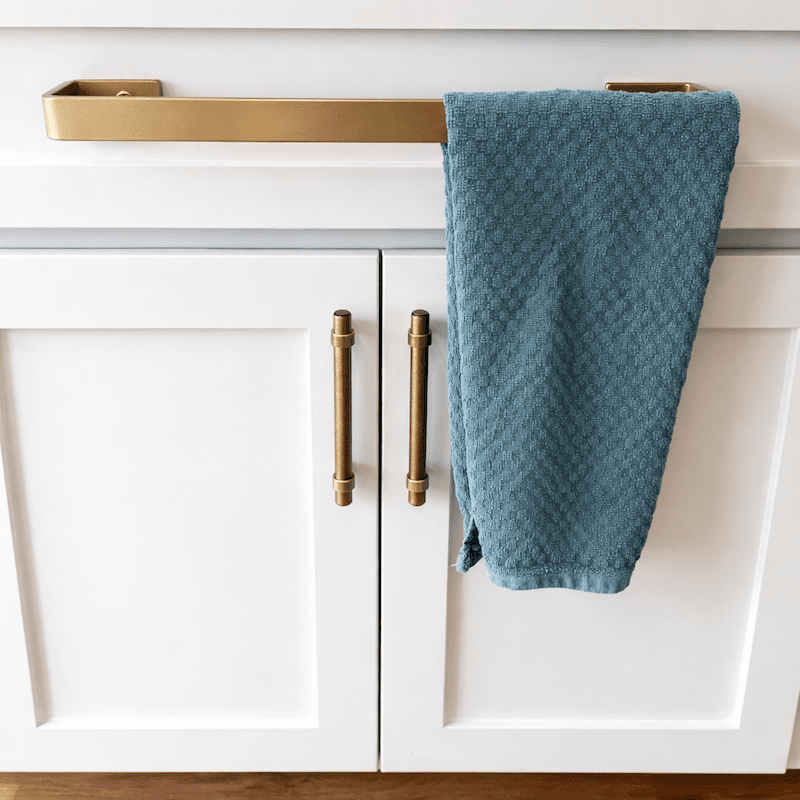 White kitchen cabinet with brass kitchen towel bar mounted on top drawer front with towel hanging