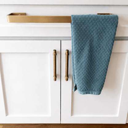 White kitchen cabinet with brass kitchen towel bar mounted on top drawer front with towel hanging