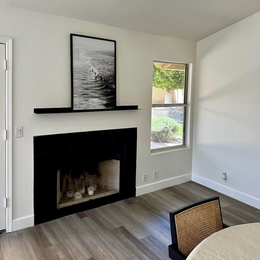 Living room with black fireplace, framed picture above, and window showing greenery.