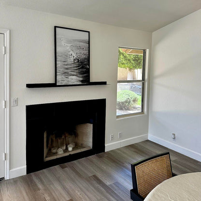 Living room with black fireplace, framed picture above, and window showing greenery.