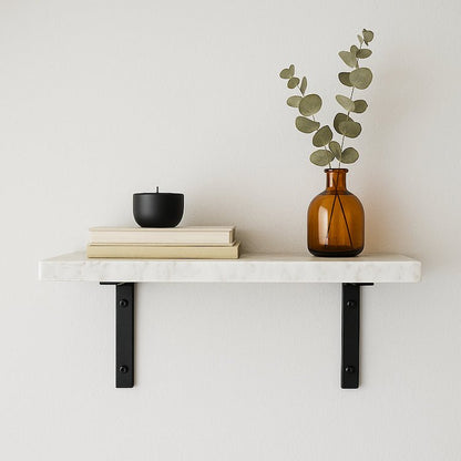 White marble shelf with books, a black candle, and an amber glass vase with greenery on a light gray background