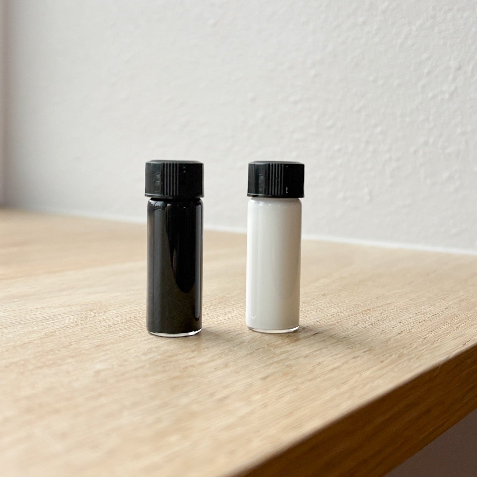 Two small glass jars with black lids on a wooden surface.