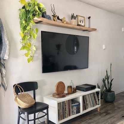 Living room with a TV mounted on the wall, a shelf with decorative items, and a chair.