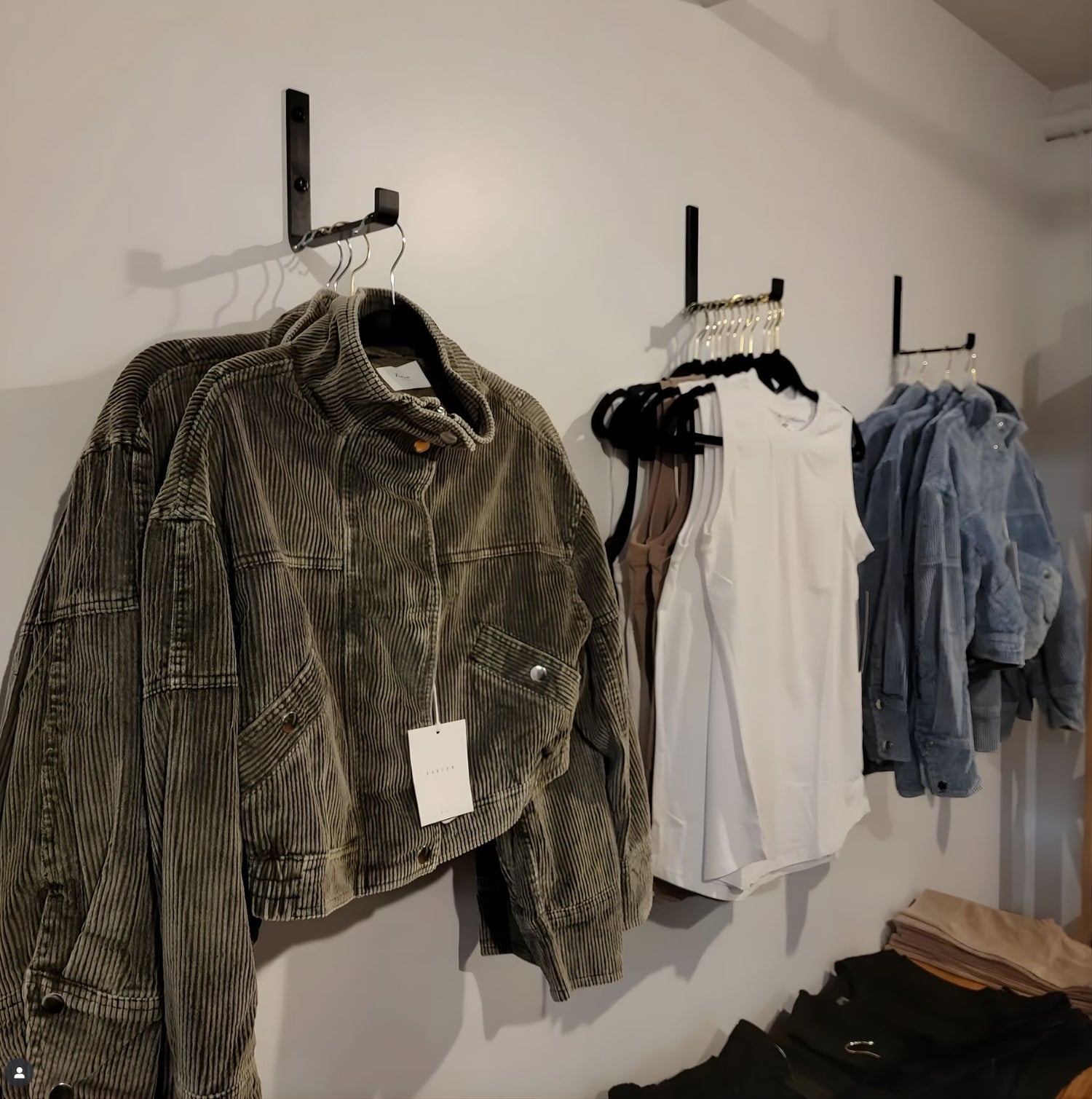 Clothing items including jackets and shirts hanging on a wall with a metal bracket hook with a neutral background.