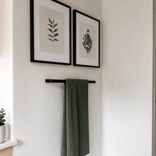 Green towel hanging on a black rack with framed botanical prints on a white wall.