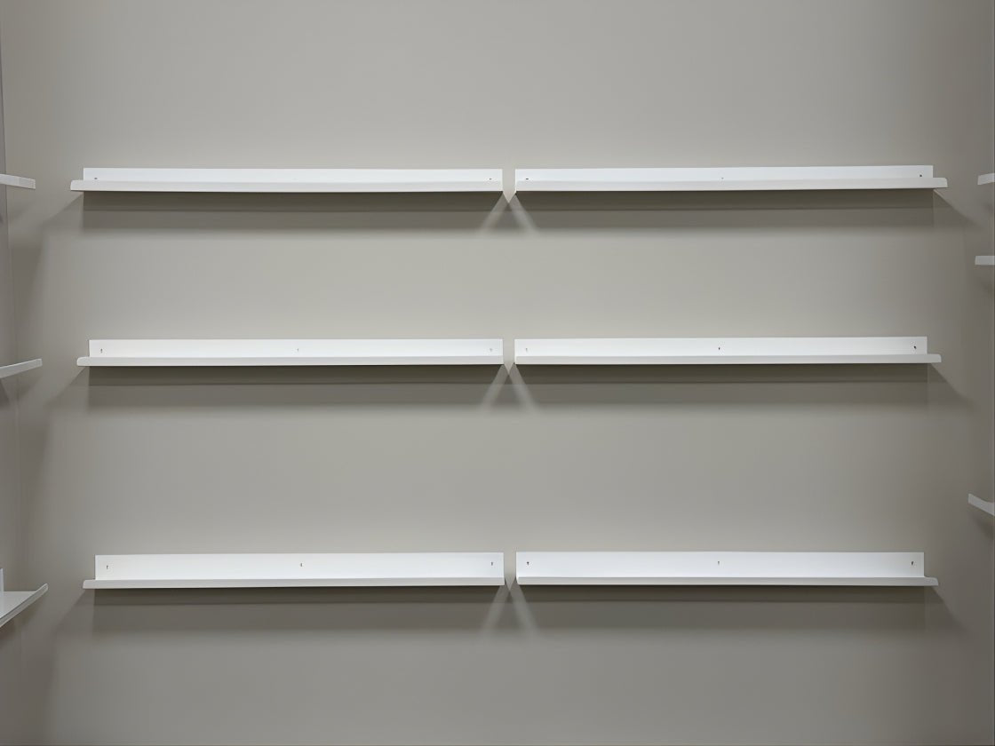 Six wall mounted white metal display ledge shelves on gray wall. Each shelf rail is empty.